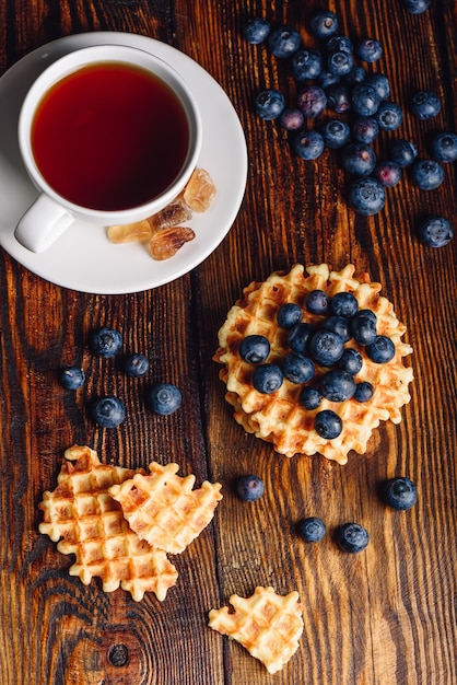 Xícara de chá com mirtilos e waffles belgas inteiros e partidos na mesa de madeira