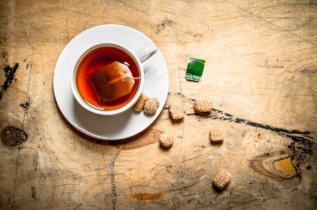 Xícara de chá e açúcar de cana na mesa de madeira.