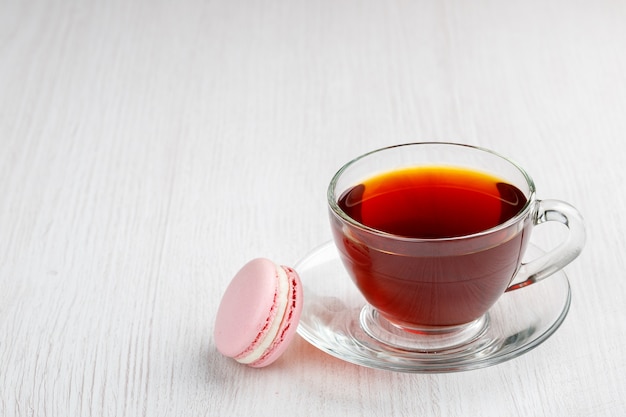 Xícara de chá e biscoito rosa sobre fundo claro de madeira
