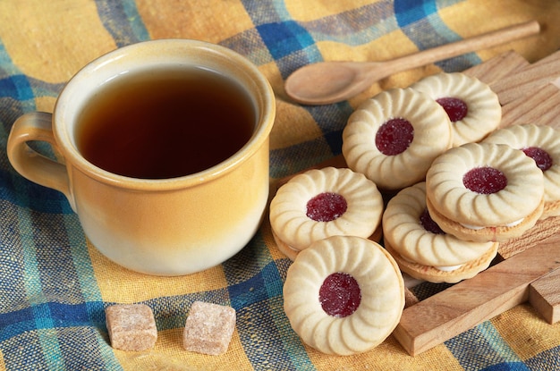 Xícara de chá e biscoitos com geléia no café da manhã na toalha de mesa