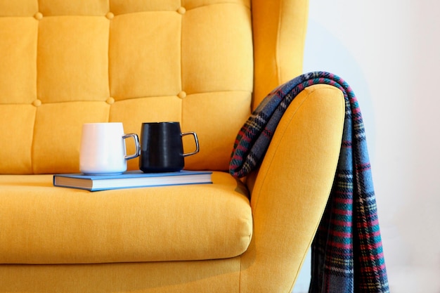 Xícara de chá e livro azul na carruagem amarela com detalhes aconchegantes do cobertor no interior da casa da sala de estar