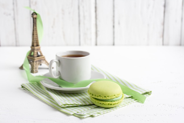 Xícara de chá e macaroons de francês verdes em um branco de madeira