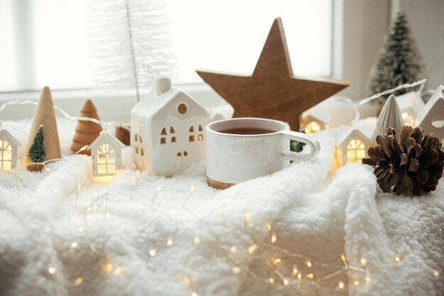 Xícara de chá elegante com casas de Natal modernas pinha estrela de madeira e decoração de árvore luzes douradas em cobertor quente no parapeito da janela Natal aconchegante estilo escandinavo fundo de Natal