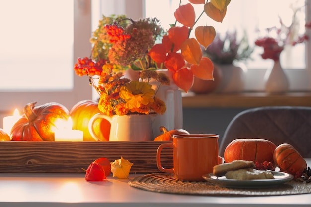 Xícara de chá laranja e decoração de outono com flores de abóbora e velas acesas na mesa