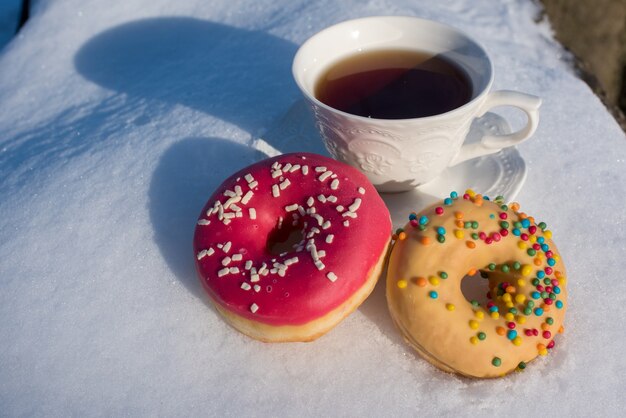 Xícara de chá no café da manhã com donuts no fundo de neve