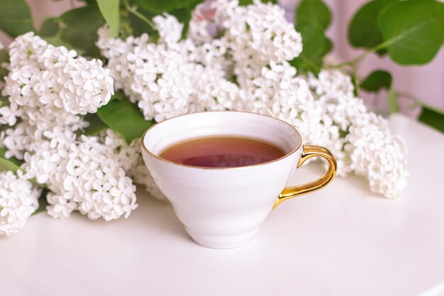 Xícara de chá quente com buquê de flores na mesa branca