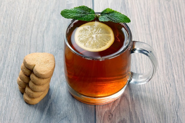 Xícara de chá transparente com limão, hortelã e biscoitos em uma mesa de madeira