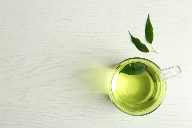 Xícara de chá verde aromático e folhas na mesa de madeira clara plana Espaço para texto