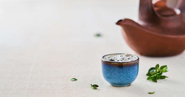 Xícara de chá verde chinês quente. Bule e folhas verdes em cima da mesa. Foco seletivo no copo. Close-up, com espaço de cópia. Ideia da festa do chá, minimalismo.