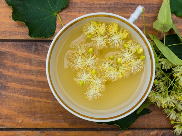 Xícara de chá verde e tília em fundo de madeira, conceito de medicina popular de flores de tília úteis