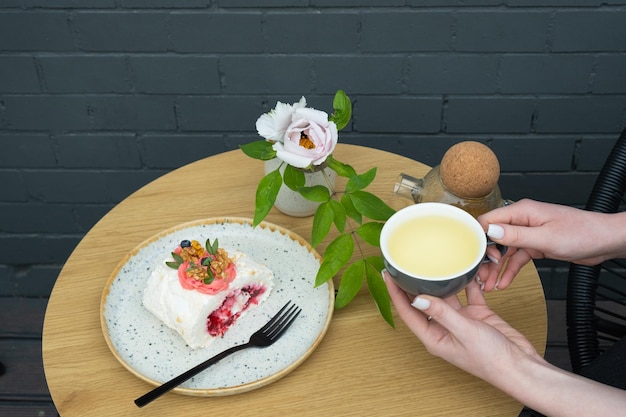 Xícara de chá verde nas mãos e um rolo de merengue na mesa do café Comida doce Natureza morta