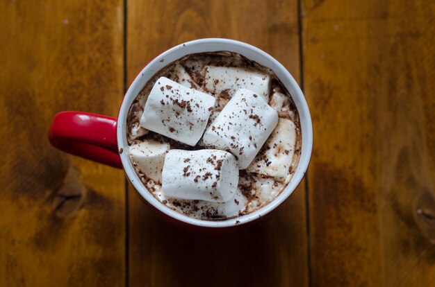 Xícara de chocolate quente com canela e marshmallows em fundo de madeira