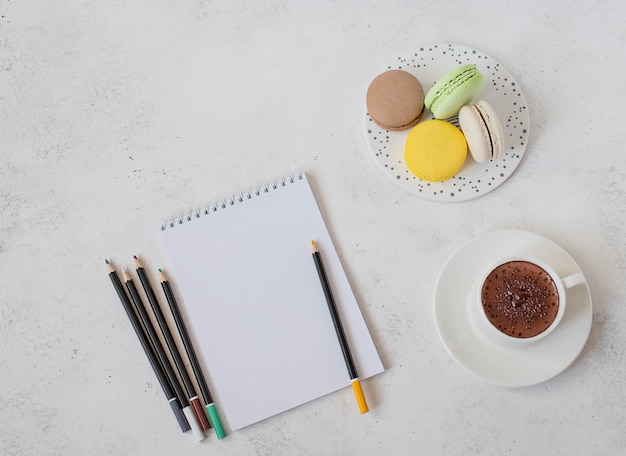 Xícara de chocolate quente com macaron, caderno e lápis