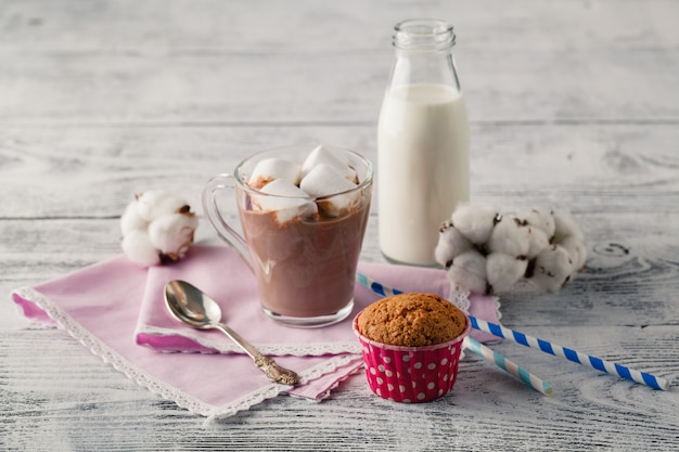 Xícara de chocolate quente com marshmallows, canela e chocolate na mesa de madeira