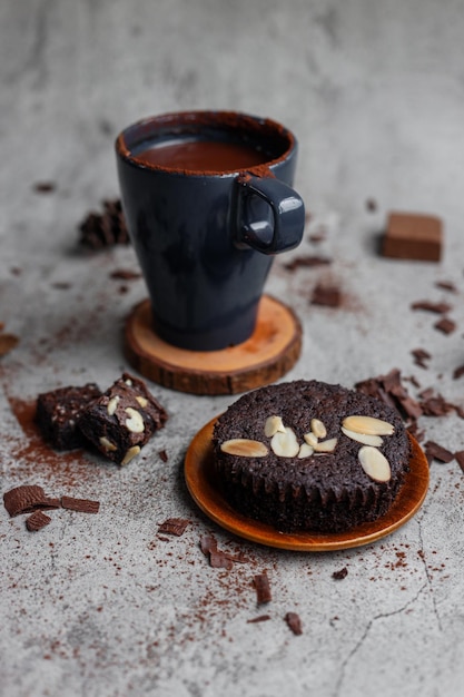 Xícara de chocolate quente e pedaços de brownie de chocolate sobre fundo claro de concreto