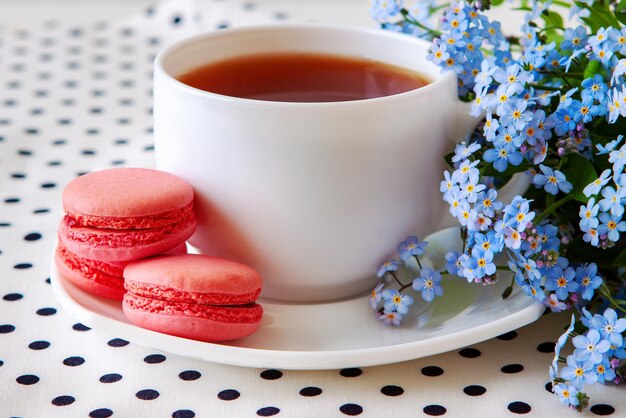 Xícara de macarons de chá e morango com um buquê de closeup de esquecidos selvagens