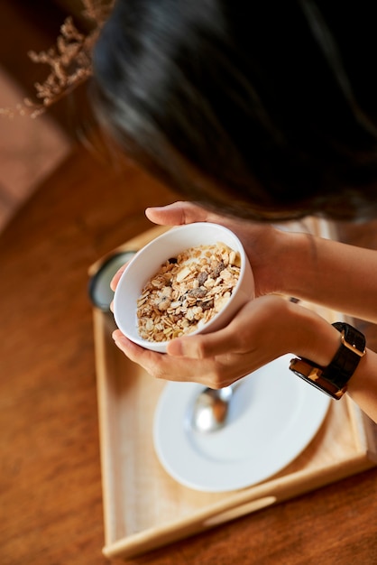 Xícara de muesli com nozes e passas nas mãos de uma jovem, vista de cima