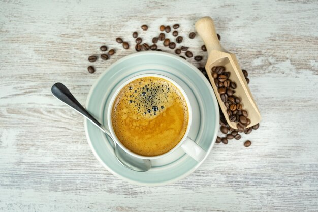 Xícara de porcelana branca com café espresso acabado de fazer e grãos de café em cima da mesa