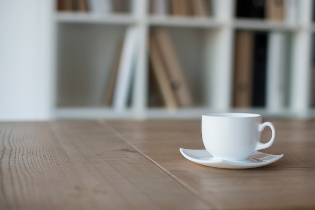 Xícara e Pires brancos com café na mesa de madeira no escritório.