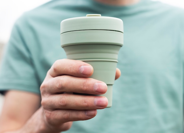 Xícara ecológica reutilizável para café para viagem. Mão masculina com caneca de chá de silicone sustentável. Pessoa amiga do ambiente.