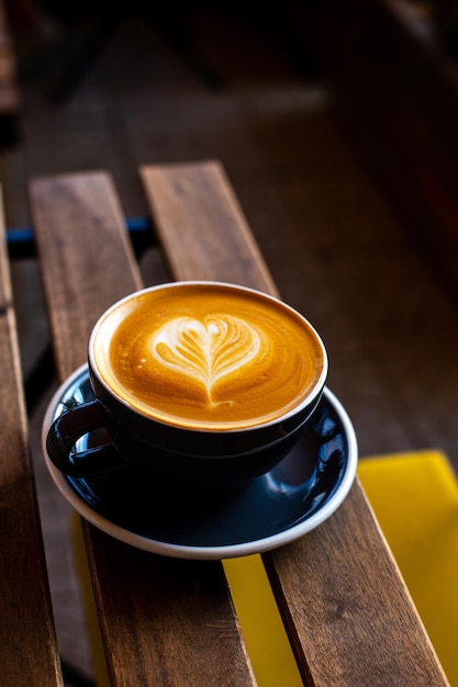 Xícara preta de cappuccino com latte art em fundo de madeira