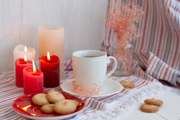 xícara quente de chá preto em uma toalha de mesa listrada, velas de cera, um vaso de vidro com ervas decorativas