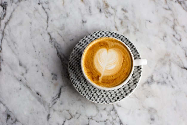 Xícara rosa na moda de cappuccino quente no fundo da mesa de mármore Arte com leite em forma de coração para símbolo de amor