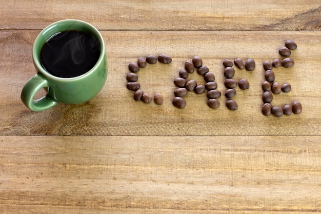 Xícara verde de café quente na mesa de madeira com a palavra café escrita em português com vista superior de grãos de café