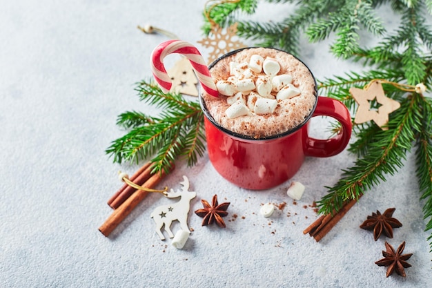 Foto xícara vermelha de chocolate quente com marshmallows e bastões de doces com árvore de natal