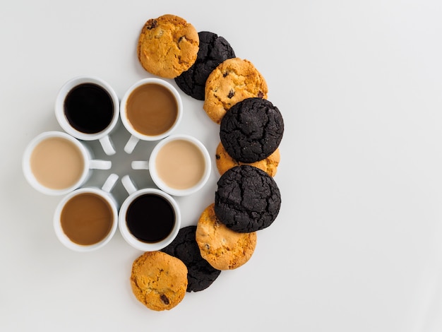 Xícaras de café colocadas em um círculo e biscoitos diferentes.