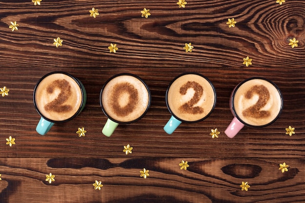 Foto xícaras de café com leite ou cappuccino de ano novo com dígitos 2022 em uma mesa rústica consecutiva, vista de cima