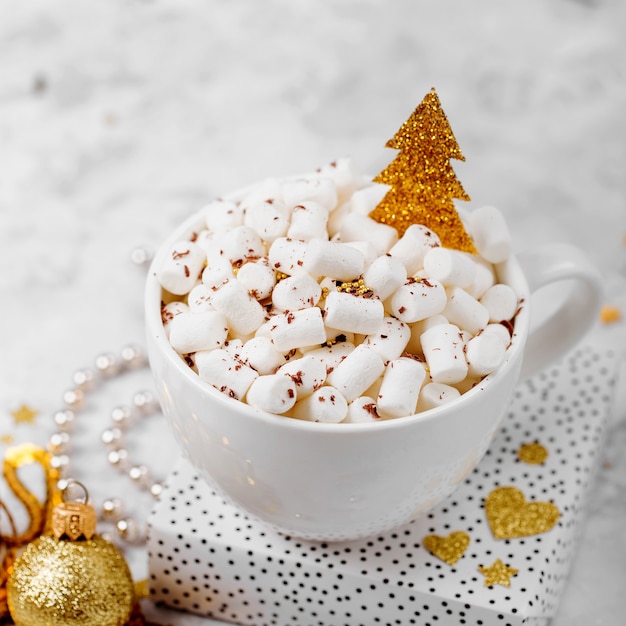 Xícaras de café com marshmallow e árvore de Natal decorativa dourada brilhante. Decoração e presentes de natal