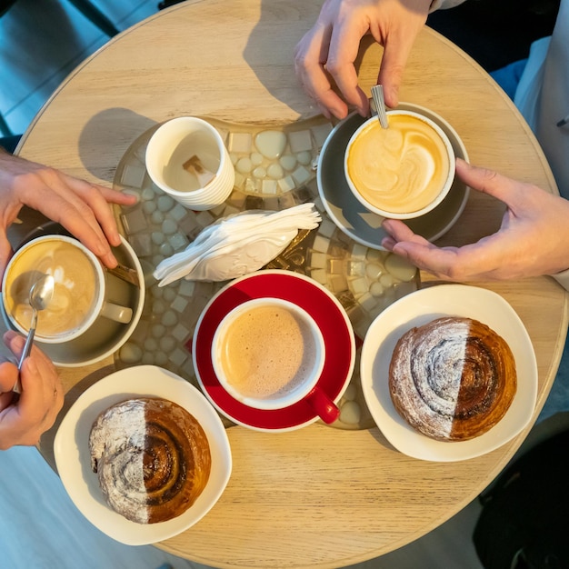 Xícaras de café e pães em uma mesa de madeira em uma cafeteria Dois caras estão segurando xícaras de cappuccino nas mãos e comendo croissants Design de interiores em um restaurante de elite