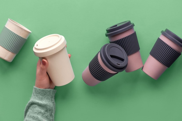 Xícaras de café ou chá reutilizáveis de viagem de bambu sortidas ou revistas com isolamento de silicone. Um copo na mão feminina. Ideia ecológica de desperdício zero para um estilo de vida sustentável