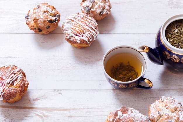 Xícaras de chá, bule e muffins na mesa de madeira branca, top close-up vista
