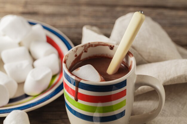 Xícaras de chocolate quente com marshmallows e paus de canela na mesa de madeira