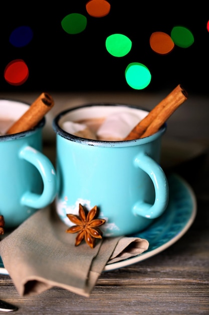 Xícaras de saboroso chocolate quente, na mesa de madeira, no fundo brilhante