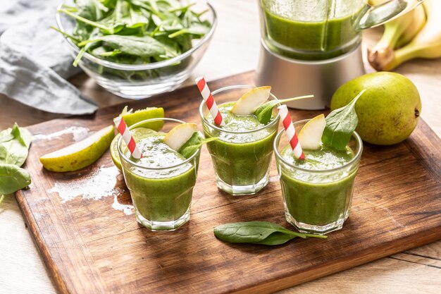 Xícaras de suco verde com canudos de papel colorido e fatias de limão em uma mesa.