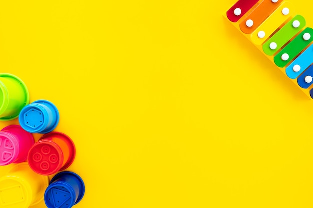 El xilófono y la pirámide de los niños del arco iris brillante en un fondo amarillo. Composición con juguetes para niños, vista superior, endecha plana, espacio de copia. Concepto de bebé, fondo.