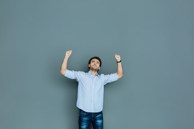 Éxito absoluto. Agradable hombre encantado positivo levantando las manos y sonriendo mientras expresa sus emociones