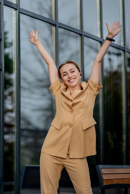 Éxito empresarial Mujer de negocios joven feliz celebrando los logros de la carrera laboral con ambas manos contra el edificio de oficinas