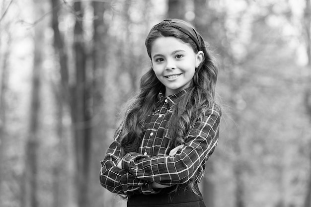 Ya en la moda Niño feliz mantener los brazos cruzados al aire libre Aspecto de moda de modelo de moda Niña pequeña usa uniforme escolar Moda de regreso a la escuela Vestuario para niños Moda y estilo