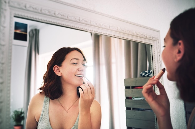 Ya sé cuál es el mejor atuendo para combinar con este color. Captura recortada de una mujer joven y atractiva que se pinta los labios mientras está de pie frente al espejo en su dormitorio en casa.