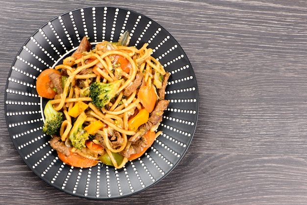 Yakisoba en un plato negro sobre una mesa