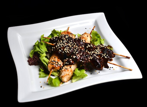 Yakitori com sementes de gergelim em um prato. Carne de frango frito e fígado de galinha em close-up de varas isolado em um fundo preto. Vista do topo.