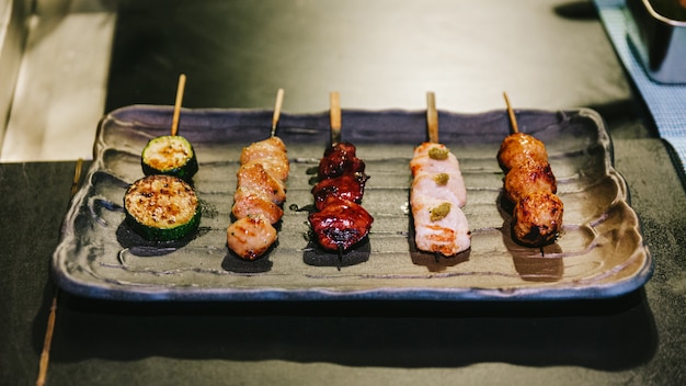 Yakitori con pollo, órgano interno y pepino servido en plato de piedra negra.