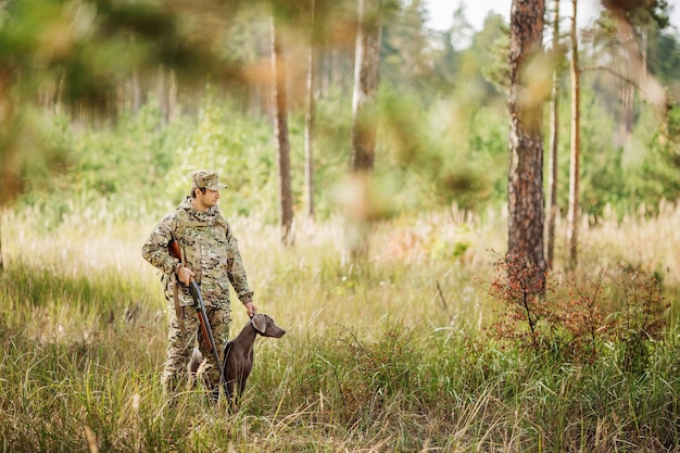 Yang hunter com rifle e cachorro na floresta