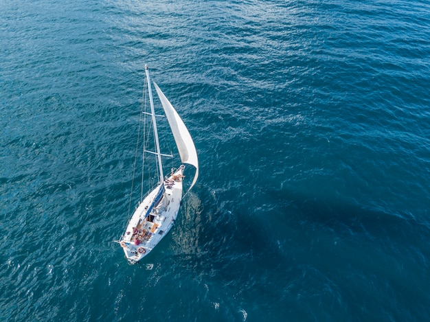 Yate aislado solo bajo la vela con el mástil alto que entra en la opinión superior aérea del mar inmóvil