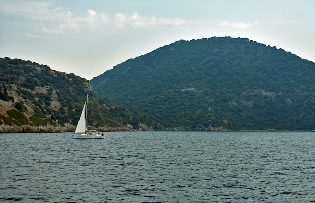 Yate navega por el mar a lo largo de las rocas.