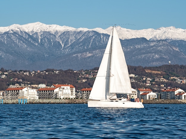 Yate de vela blanco sobre agua de mar en la costa y las montañas de fondo